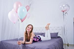 gelukkig meisje met gekleurde ballonnen op bed op kamer. verjaardag thema vieren. foto