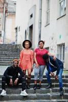 vier Afrikaanse vrienden die buiten plezier hebben. twee zwarte meisjes met jongens zitten op trappen van een oude stad. foto