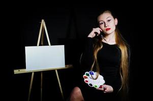 mooie vrouw kunstenaar schilder met borstels en olie canvas poseren in studio geïsoleerd op zwart. foto