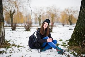 jong meisje draagt een lang groen sweatshirt, jeans en zwarte hoofddeksels met rugzak in de winterdag. foto