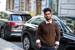 portret van jonge stijlvolle Indiase man model pose in straat tegen suv auto. foto