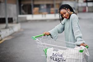 geen kunststof meer. Afrikaanse vrouw met winkelwagentje en eco-tassen poseerde buitenmarkt. foto