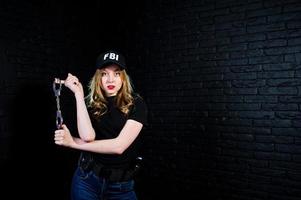 FBI vrouwelijke agent in pet en met pistool in studio tegen donkere bakstenen muur. foto