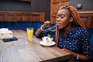 portret van mooie jonge Afrikaanse zakenvrouw met dreadlocks, draag op blauwe blouse en rok, zittend in café met ijs en ananassap. foto