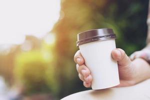 hand met papieren kopje om koffie te drinken op natuurlijk ochtendzonlicht. ruimte voor uw logo. laat ruimte voor het schrijven van tekst. foto