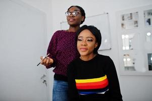 Afro-Amerikaanse vrouw die make-up toepast door visagist bij beauty salon. foto