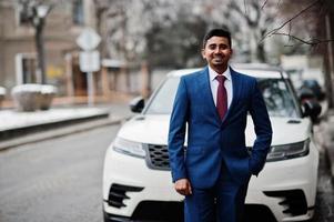 elegante Indiase modieuze man model op pak gesteld op winterdag tegen witte zakelijke suv auto. foto