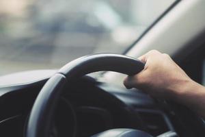 close-up van de hand houden stuurwiel jonge man besturen van een auto rijden op de weg. chauffeur reis van reizen. foto