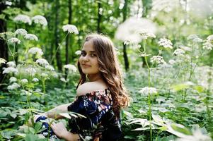 portret van een fantastisch jong meisje in mooie jurk met stijlvol krullend kapsel poseren in het bos of park. foto