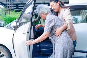 verzorger helpt aziatische bejaarde vrouw met een handicap om in haar auto te stappen, medisch concept. foto