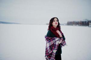 brunette meisje in groene trui en rode sjaal met geruite buiten bevroren meer op avond winterdag. foto