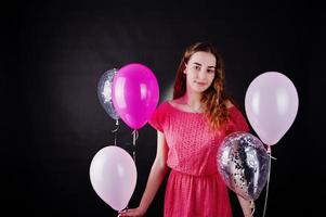 jong meisje in rode jurk met ballonnen tegen zwarte achtergrond op studio. foto