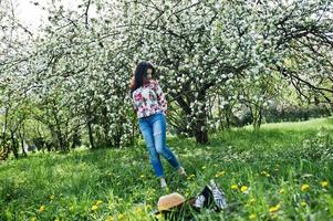 lente portret van brunette meisje in roze bril en hoed op groene bloesem tuin. foto