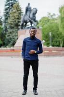 Afrikaanse man poseerde in de straat van de stad, droeg een blauw shirt en een zwarte broek. foto