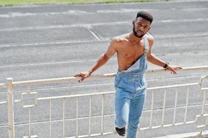 knappe sexy Afro-Amerikaanse naakte torso man op jeans overall gesteld in het stadion. modieuze zwarte man portret. foto