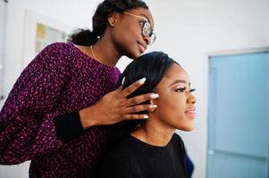Afro-Amerikaanse vrouw die make-up toepast door visagist bij beauty salon. foto