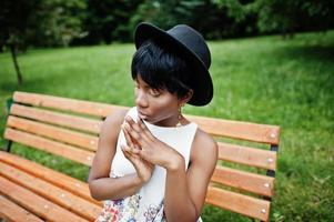 geweldige Afro-Amerikaanse model vrouw in groene broek en zwarte hoed gesteld op bankje in het park. foto