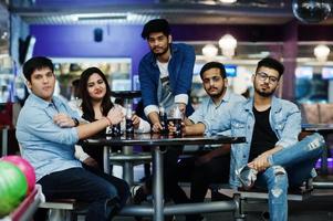 groep van vijf Zuid-Aziatische volkeren die rust en plezier hebben in de bowlingclub, op tafel zitten en frisdrank drinken bij glazen flessen. foto