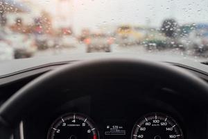 druppels regen motregen op de glazen voorruit in de avond. straat in de zware regen. bokeh achterlicht en verkeerslichten in de stad. rijd alstublieft voorzichtig met de auto, gladde weg. zachte focus. foto