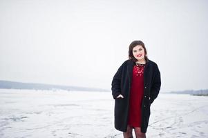 brunette plus size model op rood tegen bevroren meer op winterdag. foto