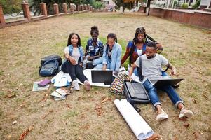 groep van vijf afrikaanse studenten die samen tijd doorbrengen op de campus op de universiteitswerf. zwarte afrovrienden die op gras zitten en met laptops studeren. foto