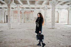 brunette stijlvolle casual meisje in sjaal en handtas tegen verlaten fabrieksplaats. foto