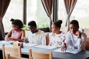 gelukkige Afrikaanse vrienden zitten en chatten in café. groep zwarte mensen die in restaurant samenkomen en naar hun mobiele telefoon kijken. foto