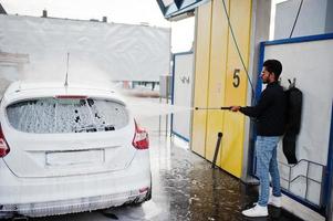 Zuid-Aziatische man of Indiase man die zijn witte transport op autowasserette wast. foto