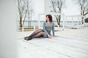 portret van brunette meisje in grijze jurk zit op witte houten constructie. foto