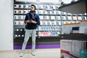 indiase baard man klant koper bij mobiele telefoon winkel luister muziek van draadloze oortelefoons verbinding maken met zijn smartphone. Zuid-Aziatische volkeren en technologieën concept. gsm winkel. foto