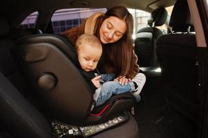 jonge moeder en kind in auto. kinderzitje op stoel. veiligheid rijden concept. foto