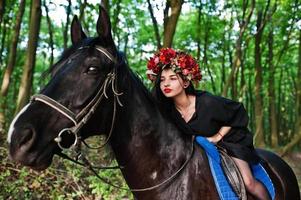 mystieke meisje in krans slijtage in het zwart bij paard in hout. foto