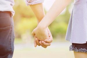 paar liefhebbers romantisch hand in hand naar de zon met felle zon flare in openbare parken, of close-up in een conceptueel beeld eerste liefde adolescente jonge relatie. foto