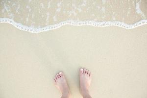 close-up van de blote voeten van een man staan nat op het strand, met een zandrand eronder zachtjes. vakantie op oceaanstrand, voet op zeezand. laat lege kopie ruimte voer de tekst hierboven in. reis foto