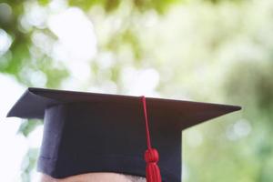 afstuderen, close-up student hoed en kwast oranje in tijdens aanvang succes afgestudeerden van de universiteit, concept onderwijs felicitatie. afgestudeerde student universitair diploma. foto