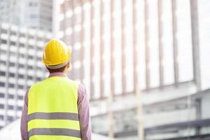 achteraanzicht van technische man bouwvakker draag een veiligheidshelm en draag reflecterende kleding voor de veiligheid van het werk. ingenieur staande op zoek naar projectsucces.