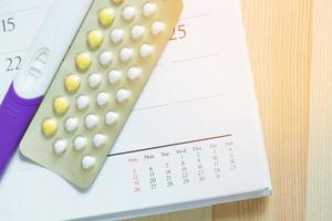 positieve zwangerschapstest en anticonceptiepillen op datum van kalenderachtergrond. gezondheidszorg en geneeskunde anticonceptie. foto