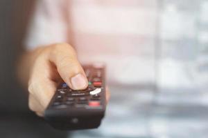 close-up televisie afstandsbediening in casual man handen wijzend naar tv-toestel en het in- of uitschakelen. selecteer kanaal tv kijken op zijn bank thuis in de woonkamer ontspannen. foto