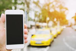 mensen van hand houden tonen witte mobiele smartphone met leeg leeg scherm. ruimte voor tekst of applicatie die het autoconcept belt. autoparkeerplaats in rij aan de kant van de wegachtergrond foto