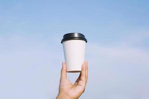 hand met papieren kopje om koffie te drinken op de achtergrond van de stad, natuurlijk ochtendzonlicht. ruimte voor uw tekst of logo. foto