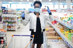 afrikaanse vrouw met een medisch wegwerpmasker en handschoenen die in de supermarkt winkelt tijdens de uitbraak van coronaviruspandemie. epidemische tijd. foto