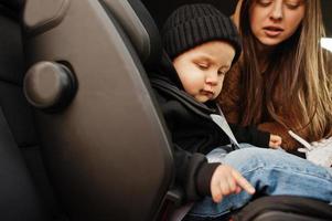 jonge moeder en kind in auto. kinderzitje op stoel. veiligheid rijden concept. foto