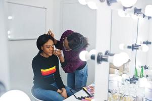 Afro-Amerikaanse vrouw die make-up toepast door visagist bij beauty salon. foto