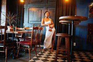 Afro-Amerikaanse vrouw, retro kapsel in witte jurk in restaurant. foto