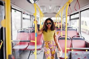 jonge stijlvolle Afro-Amerikaanse vrouw in moderne zonnebril rijden op een bus. foto