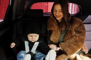 jonge moeder en kind in auto. kinderzitje op stoel. veiligheid rijden concept. foto