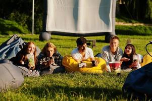 jonge multi-etnische groep mensen kijken naar film op poef in openluchtbioscoop. foto