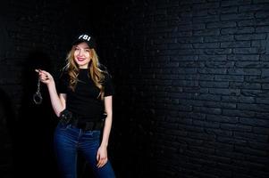 FBI vrouwelijke agent in pet en met pistool in studio tegen donkere bakstenen muur. foto