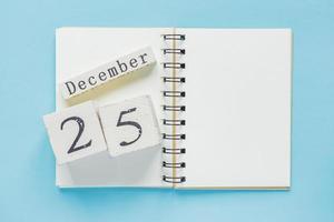 25 december op een houten kalender op een leerboek op blauwe achtergrond. kerst en nieuwjaar concept foto