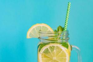 mason jar glas zelfgemaakte limonade met citroenen, munt en papierstro op turkooizen achtergrond. zomer verfrissend drankje. foto